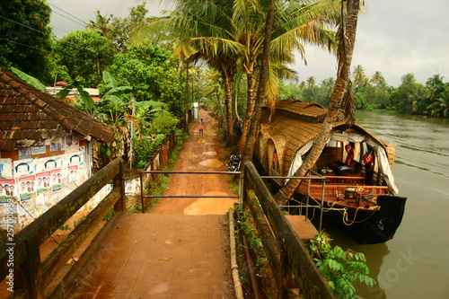 Houseboat with man walking and sandy wet path at Backwaters India