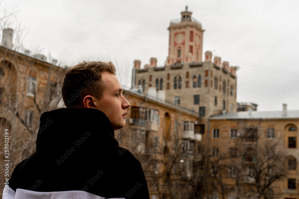 back view of attractive male person in hoodie looking on city building in a moody weather
