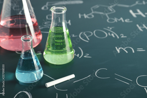 Laboratory glassware on blackboard with chemical formulas, closeup
