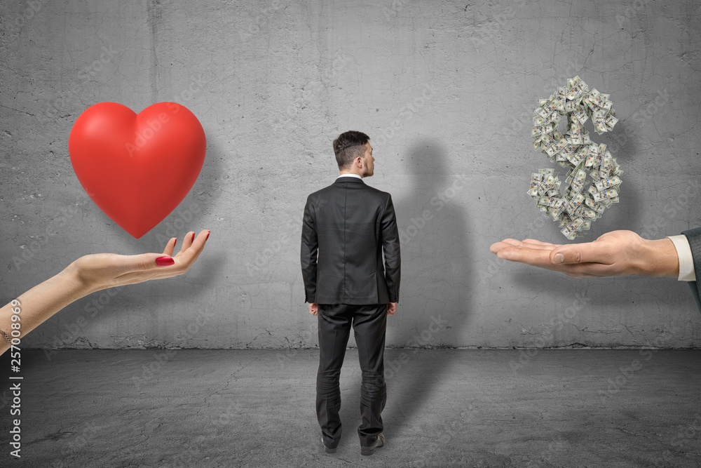 Fototapeta premium Businessman standing between hand holding red heart and hand holding money dollar sign on grey wall background