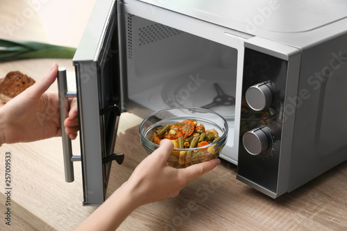 Young woman using microwave oven on table in kitchen