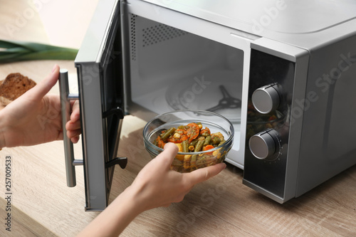 Young woman using microwave oven on table in kitchen photo