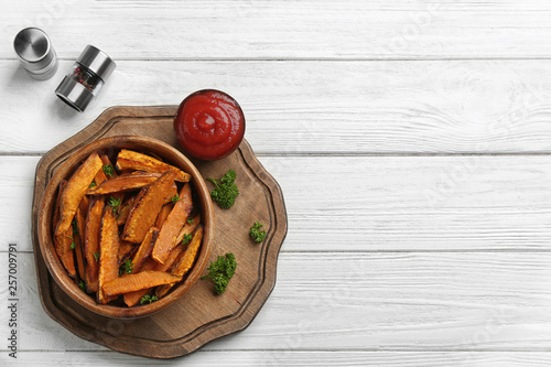 Bowl with tasty sweet potato fries on wooden background, top view. Space for text