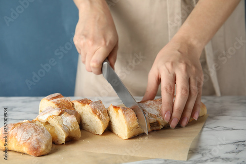 Woman cutting bread on marble table, closeup