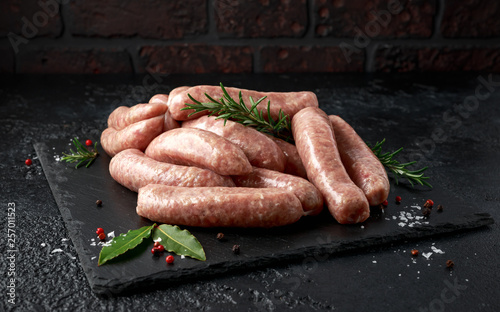 Foto Freshly made raw butchers sausages in skins with herbs on stone board