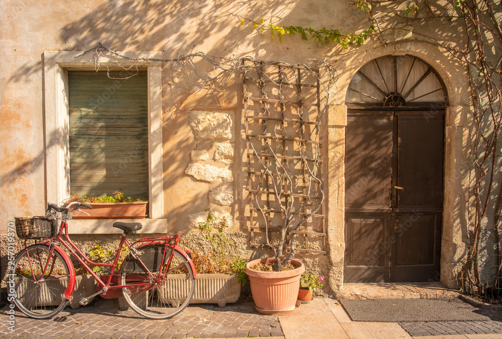 Exterior of ann old, abandoned house with a red bicycle and potted plants in a street of the medieval town of Lazise on Lake Garda, Veneto, Italy