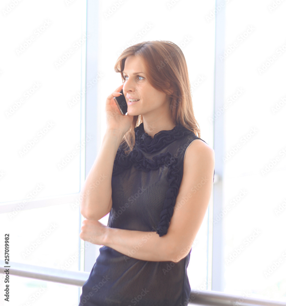 modern business woman talking on smart phone while standing near a large office window modern business woman talking on smart phone while standing near a large office window