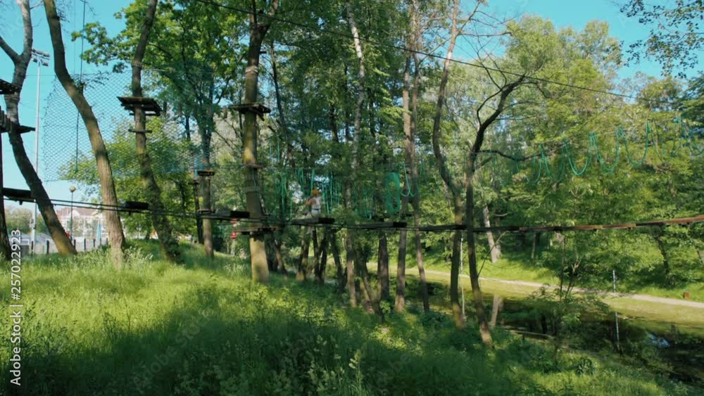 Man in Helmet is Sliding Down Zip Line in Adventure High Rope Park and Doing Climbing Exercises in Sunny Summer Day Man in Helmet is Sliding Down Zip Line in Adventure High Rope Park and Doing Climbing Exercises in Sunny Summer Day