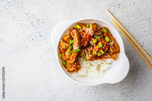 Teriyaki chicken with rice, sesame and green onions in white bowl.