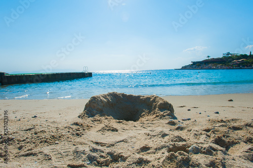 Fototapeta Naklejka Na Ścianę i Meble -  A sandcastle on a sandy beach, set against a bright blue summer sky