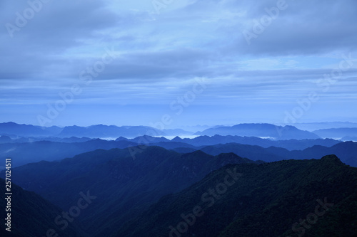 Abstract Image, Mountain Silhouettes at dawn - rolling jagged mountain peaks, cold blue hues. Panoramic Abstract Background Image, overcast skies, layers of rolling mountains in the distance.