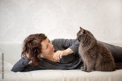 Young woman is resting on a sofa with her fluffy gray beautiful cat.