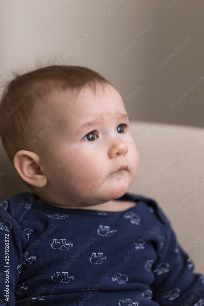 Vertical view of adorable worried looking fair baby girl in dark blue shirt sitting looking up with dark eyes
