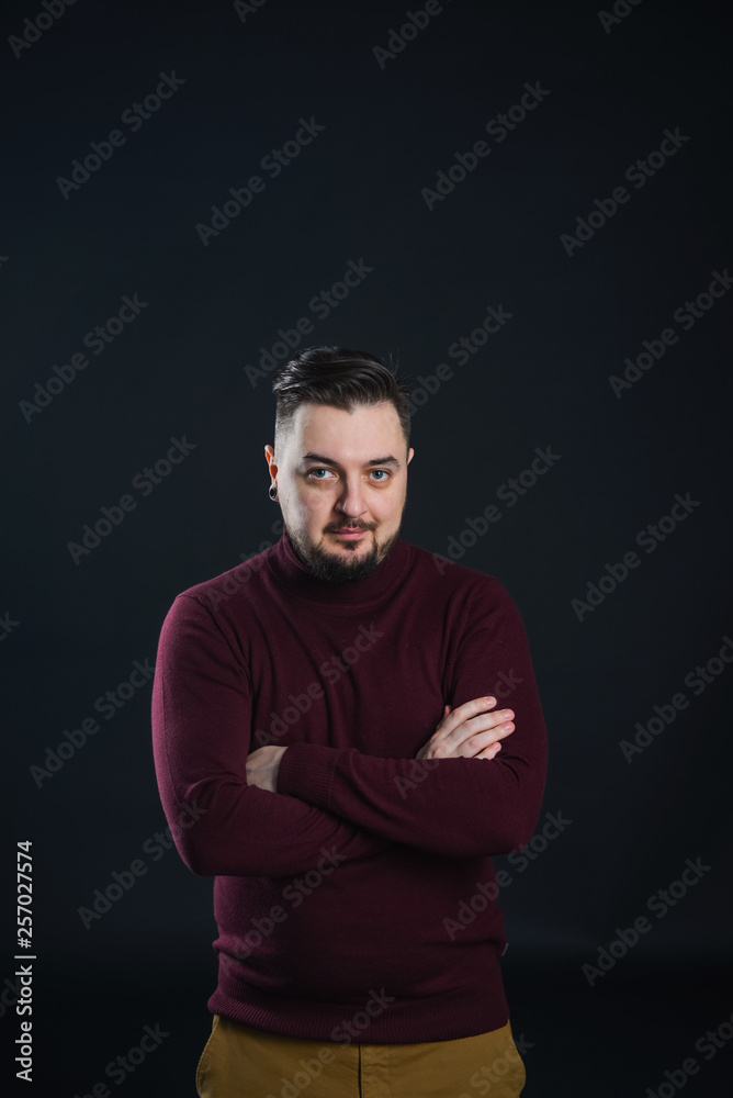 a man with a beard in casual clothes poses on an isolated dark background, in a burgundy sweater in the studio a man with a beard in casual clothes poses on an isolated dark background, in a burgundy sweater in the studio