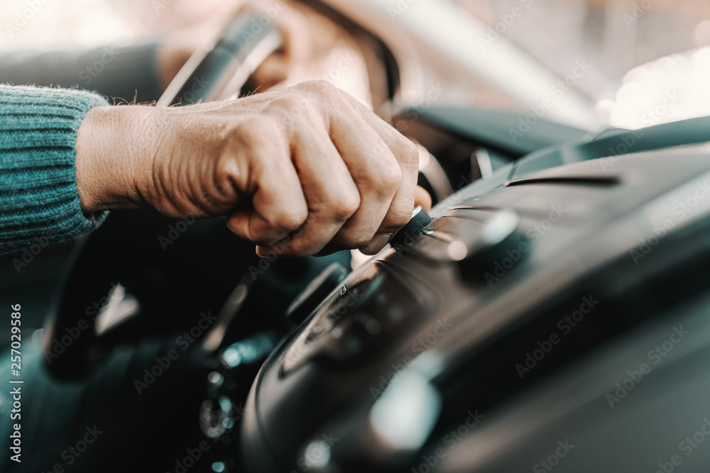 Close up of senior man changing radio station while sitting in his car. Close up of senior man changing radio station while sitting in his car.