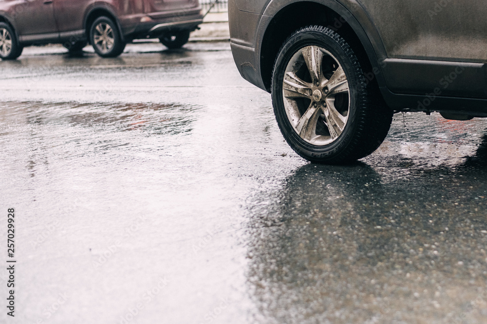 spraying water from the wheels of a car moving on a wet urban asphalt road. wet car wheel in the thaw. a car moving at speed through a puddle on a flooded city road during rain