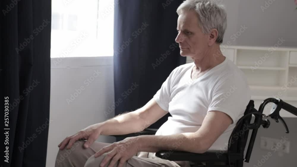 Paraplegic senior man on a wheelchair by the window Paraplegic senior man on a wheelchair by the window