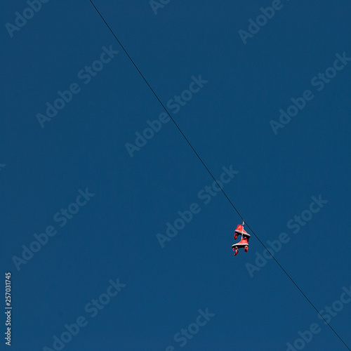 Orange roller skates hanging on a wire against blue, clear sky. Minimalistic. Square format. Contrasting colors.