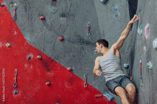 Dark-haired young man looking on the climbing wall. Fit man thinking where to move.copy space