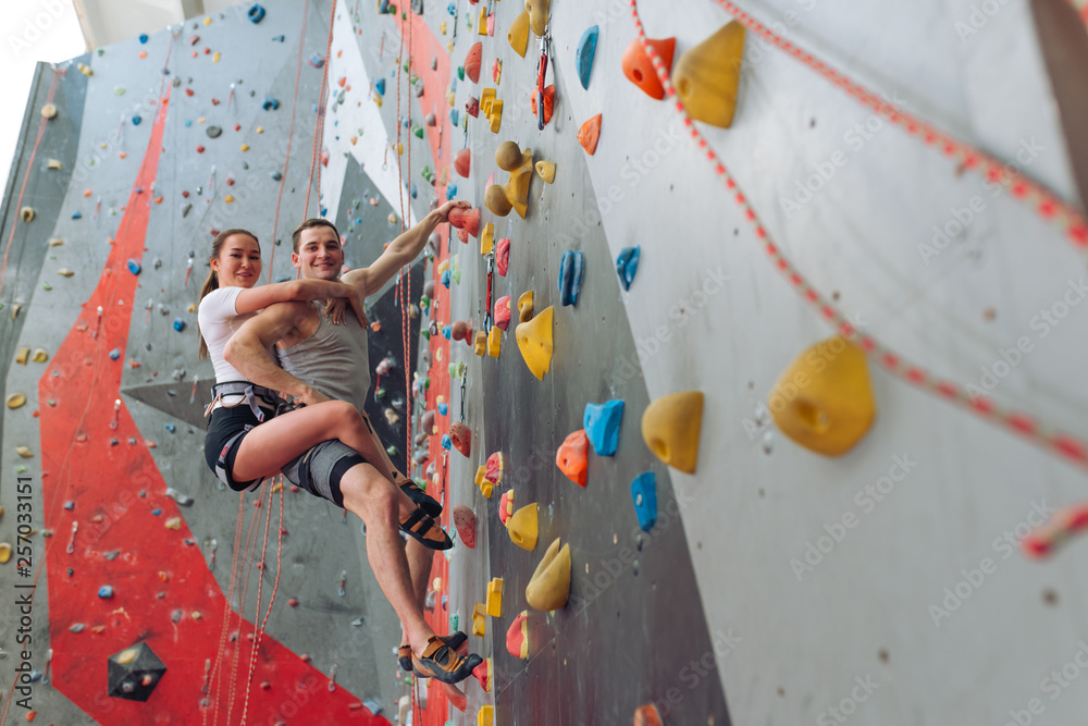 Obraz premium strong positive woman and man looking at the camera while climbing to the wall. low angle view. copy space