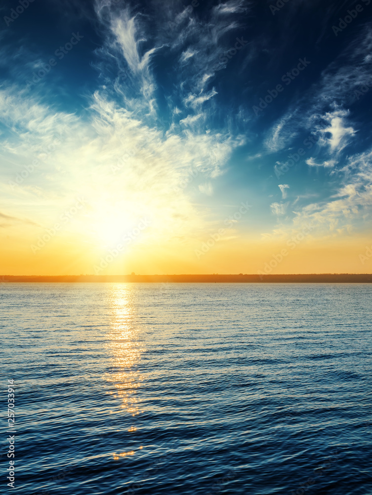 Fototapeta premium orange sunset in dark blue sky with clouds over river