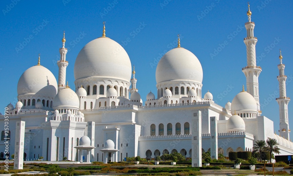 The Famous Abu Dhabi Grand Mosque during the day showing the minarets, spires, and centre dome on a beautiful blue sky day