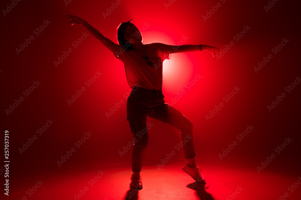 Young woman in casual urban clothes dancing gracefully, moving to hip hop music in the centre of nightclub stage. Laser show in a nightclub. Stage lights. Soffits