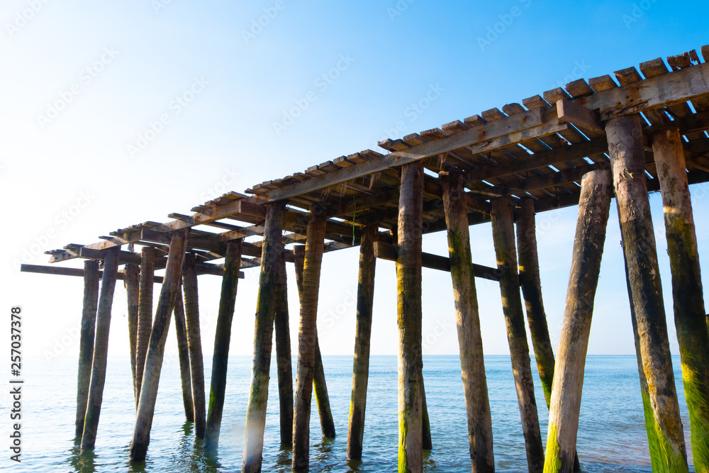 The old wooden pier stretches out into the sea with a beautiful blue sky in the background. Tourism