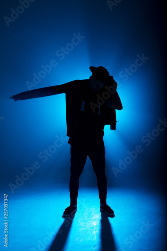 silhouette of single male break dancer isolated on blue neon background with light flare in middle