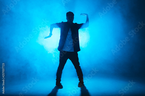 A dark silhouette of a singer on the stage, dancing alone during performance on dark blue neon background with smoke and lights.