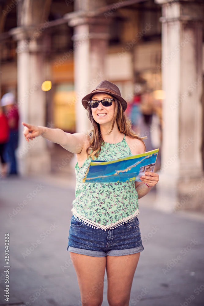 Beautiful tourist woman is seeing something very exciting. She is pointing at that direction with a map on her other hand.