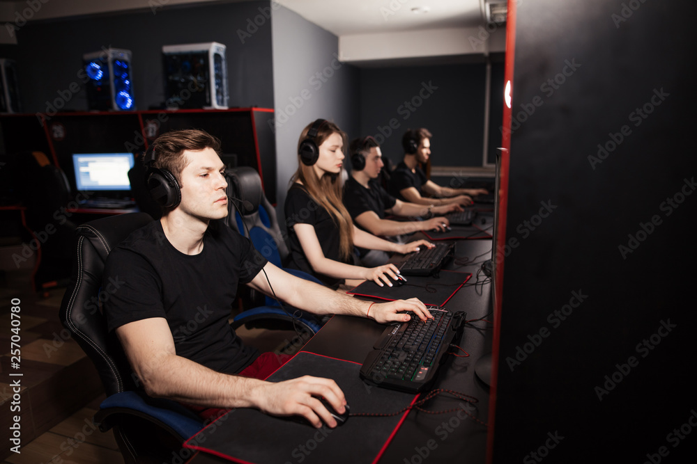 Obraz premium Young female and male gamers playing video game while spending weekend leisuretime at pc gaming club, focused serious people behind pc monitor at dark room. Entertainment or addiction concept