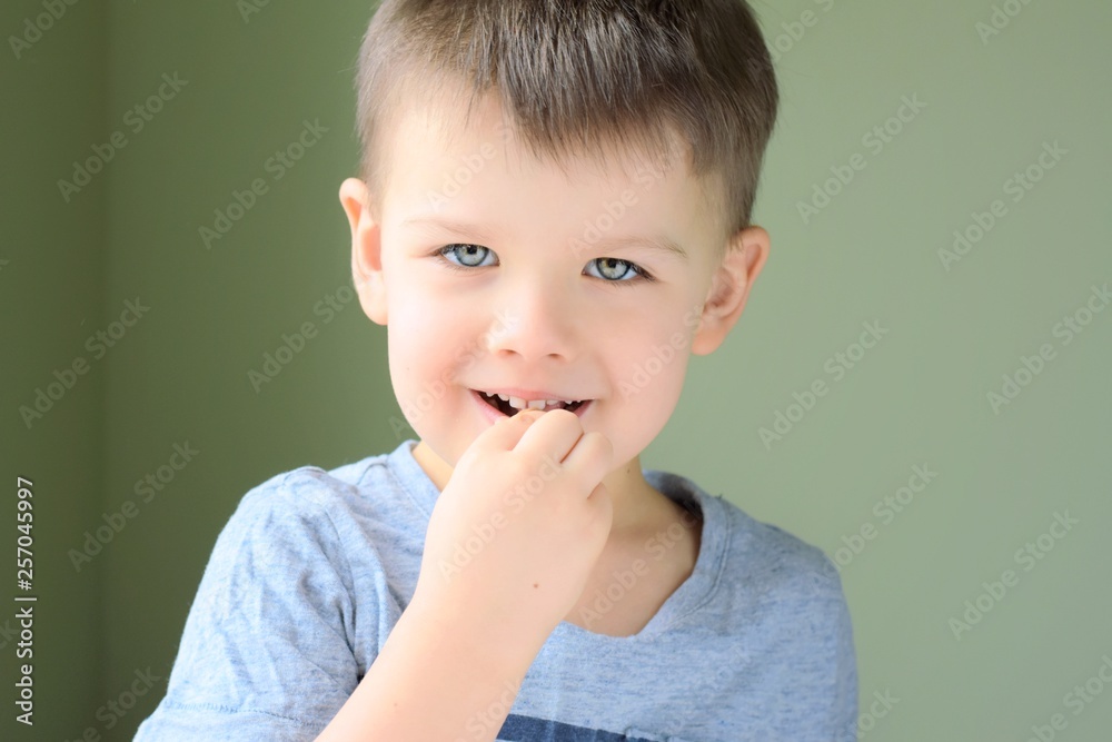 Emotional portrait of a white handsome caucasian blue eyed boy on neural blurred background. Smiling cute toddler boy eating candy. Handsome toddler boy looking at the camera and eat Emotional portrait of a white handsome caucasian blue eyed boy on neural blurred background. Smiling cute toddler boy eating candy. Handsome toddler boy looking at the camera and eat