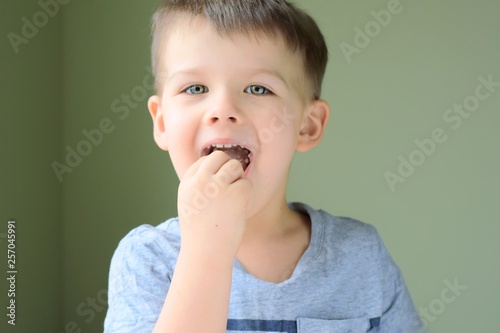 Emotional portrait of a white handsome caucasian blue eyed boy on neural blurred background. Smiling cute toddler boy eating candy. Handsome toddler boy looking at the camera and eat
