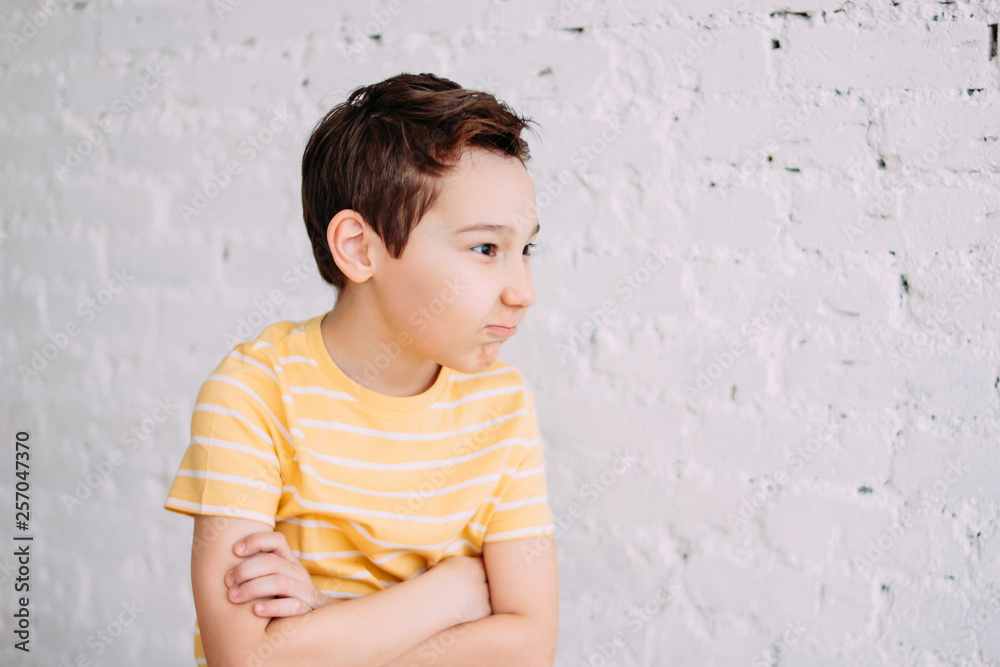 Cute tween angry boy with funny face in yellow t-shirt isolated on white brick wall background