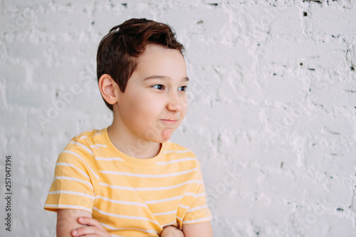 Cute tween angry boy with funny face in yellow t-shirt isolated on white brick wall background photo