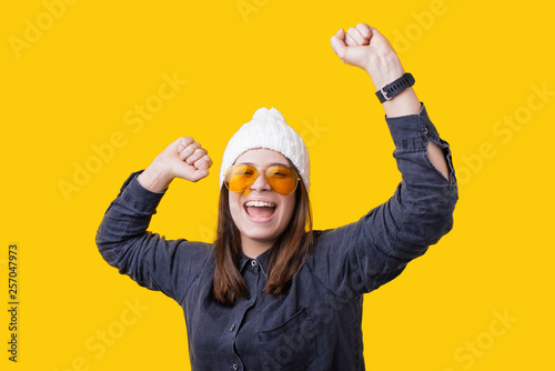 Portrait of happy cute young woman with toothy smile raised hands and celebrate achievement goal. Isolated over yellow background