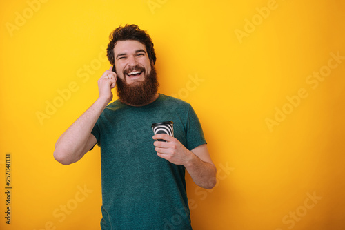 Begin your morning with cup of coffee. Handsome young man talking on mobile phone and holding cup of coffee on yellow background