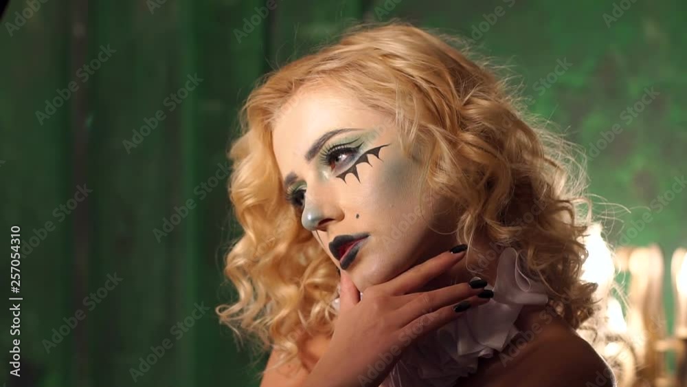 Girl teenager with bright makeup witch looks scary eyes into the camera and runs a hand over the face. Creepy image of a girl on the feast of all saints, Halloween.