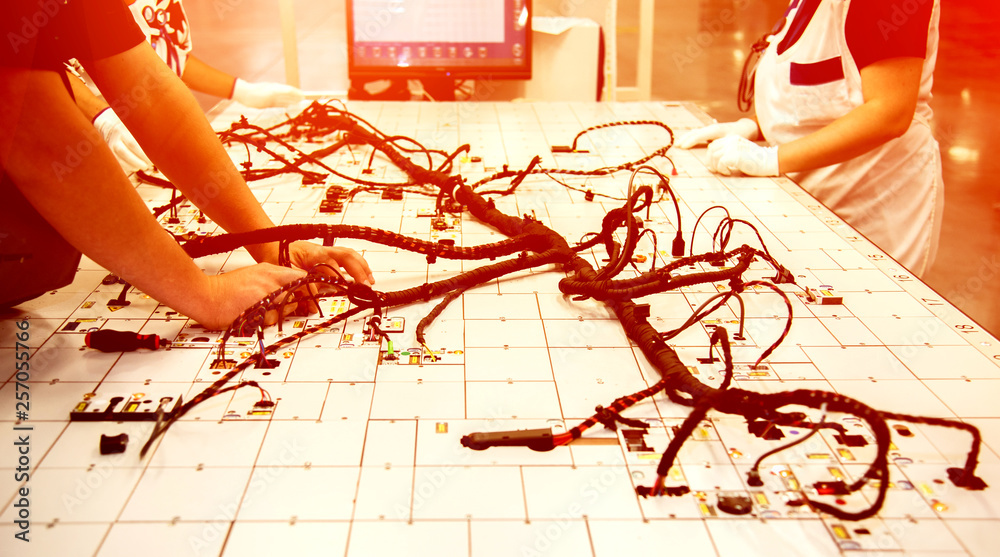 Hands of employees who check the quality of the wiring for cars at a modern plant on a special stand at the production shop