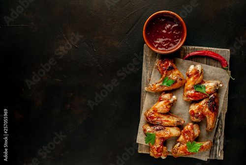 Grilled chicken wings in a barbecue sauce with parsley on a cutting board on a concrete table. Top view with copy space.