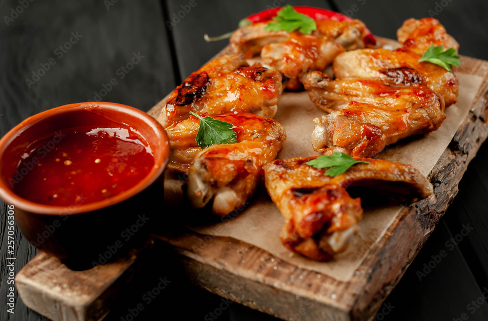 Grilled chicken wings in a barbecue sauce with parsley on a cutting board on a wooden background Grilled chicken wings in a barbecue sauce with parsley on a cutting board on a wooden background
