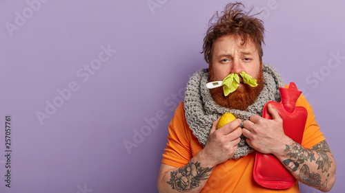 Fotografiet Photo of sick man has terrible sneezing, keeps napkins in nose, suffers from rhi