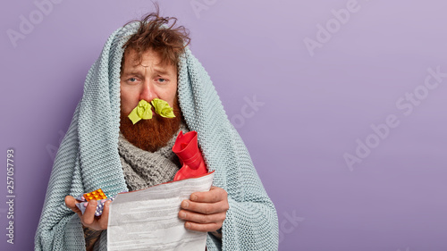 Canvas Print Indoor shot of displeased red haired guy holds medical leaflet with medicaments,