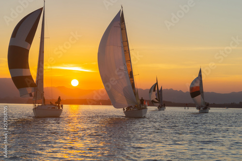 Yachts under sail and silhouette of setting sun