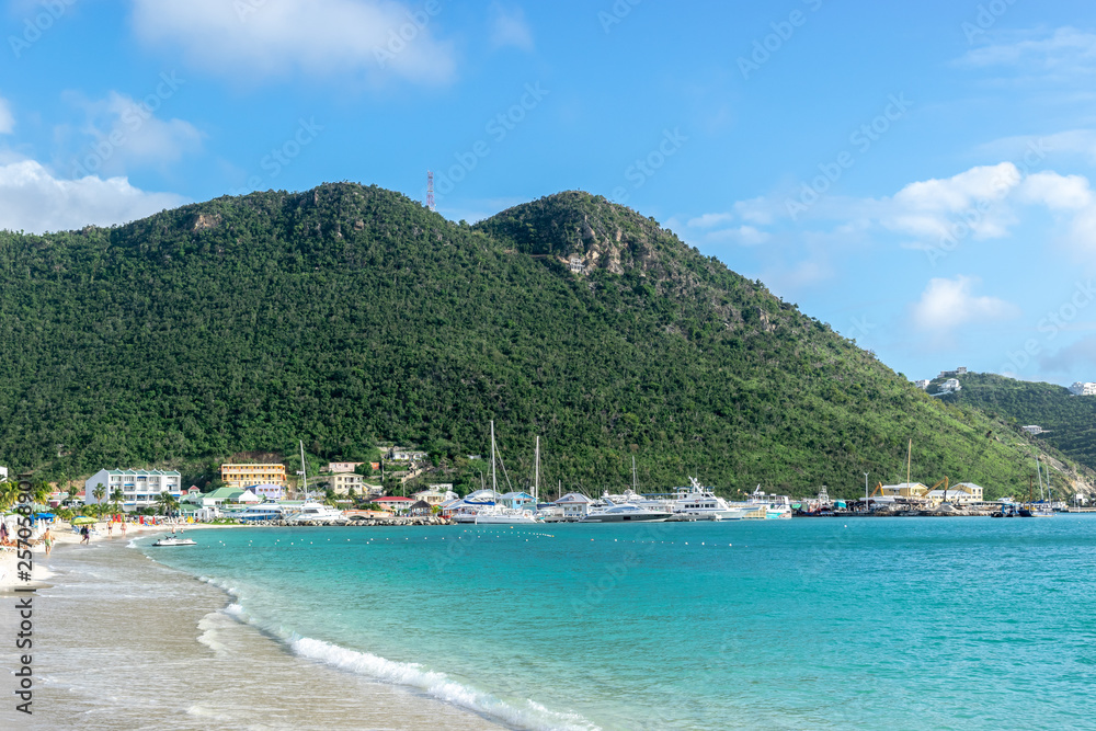 Beautiful white sand beac along coastline in Sint Maarten. Buildings, mountains and yachts in background.