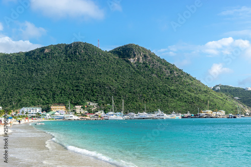 Beautiful white sand beac along coastline in Sint Maarten. Buildings, mountains and yachts in background.