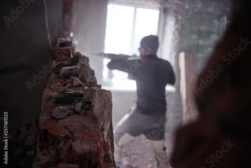 A man worker breaks a brick wall with a jackhammer, builds and repairs his house. © amixstudio