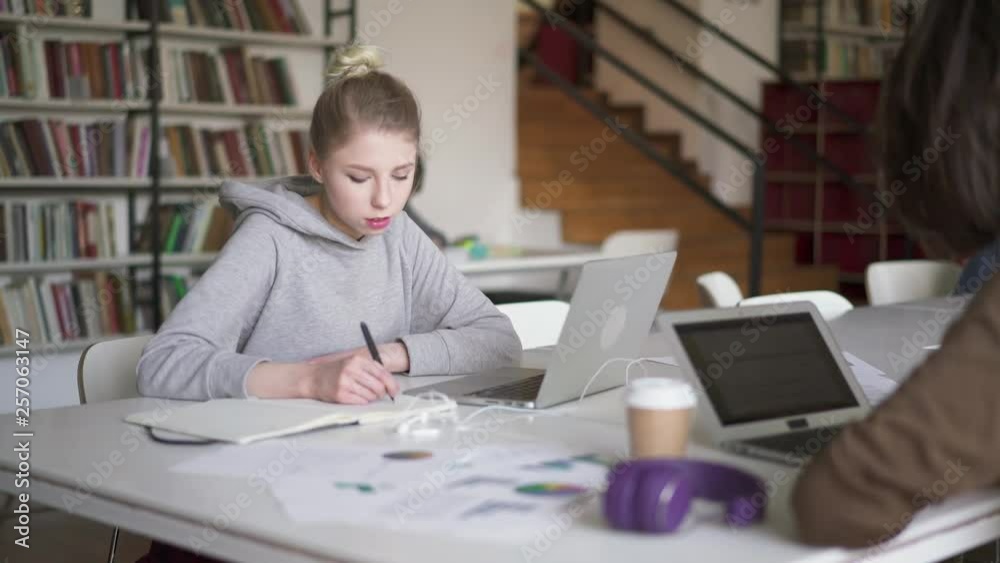 Middle pan shot of young woman student wearing grey hoodie rewrite information from laptop. Pan shot right to left of student doing exercises typing on laptop. Middle pan shot of young woman student wearing grey hoodie rewrite information from laptop. Pan shot right to left of student doing exercises typing on laptop.