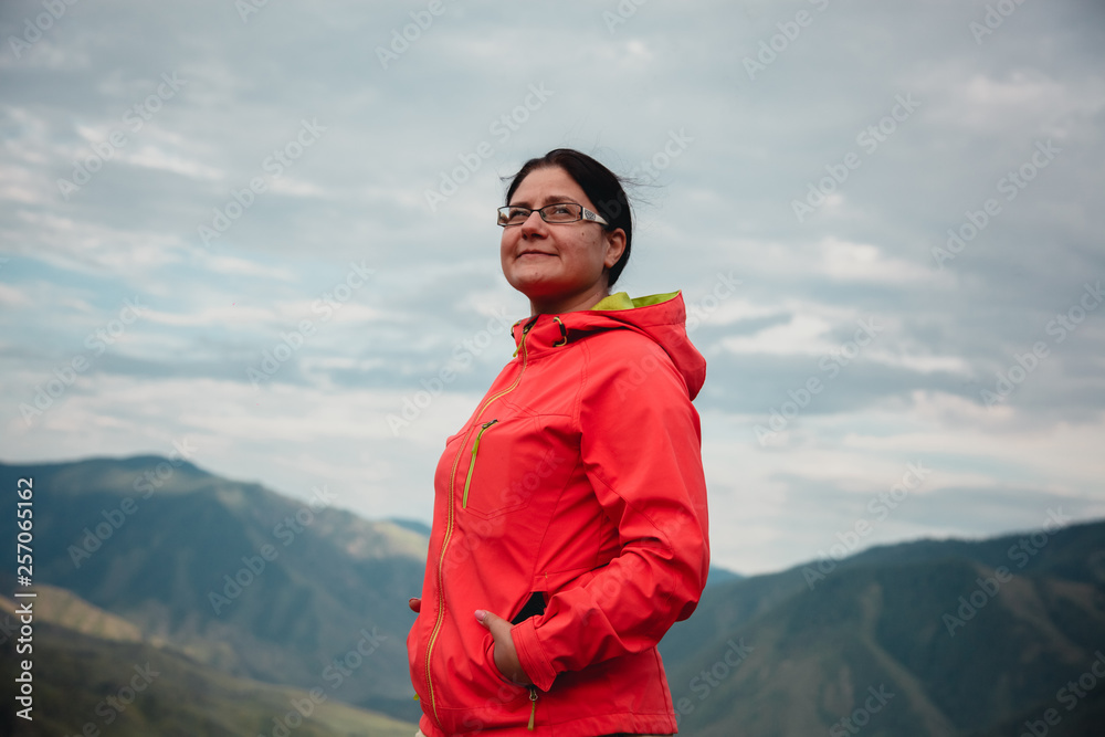 Naklejka premium Girl smiling in a red jacket sitting on the mountain. Enjoys the beautiful view around.